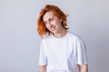Gülümseyen kızıl saçlı kadın beyaz tişört giymiş bir yerlere bakıyor.
