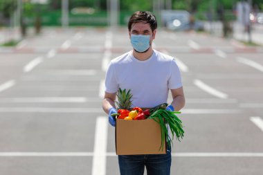   Koruyucu maskeli ve tıbbi eldivenli genç kurye paket servis yapıyor..