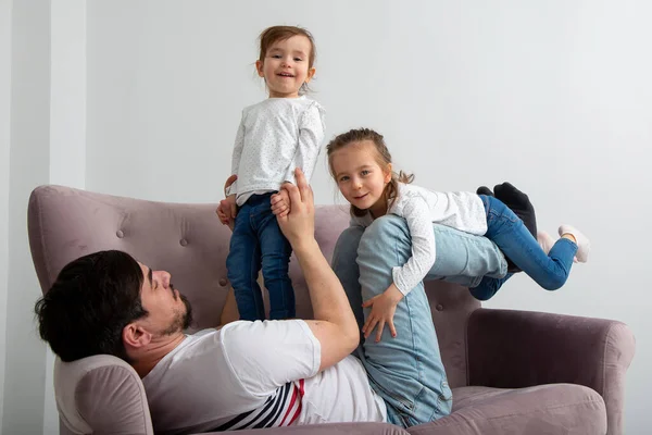 Mutlu bir aile. Genç baba, küçük tatlı kızı kaldırıyor uçak gibi uçuyor güneşli bir haftasonu kanepesinde eğleniyor, kaygısız, sevimli küçük çocuklar, anne babasıyla kanepede oynuyor.