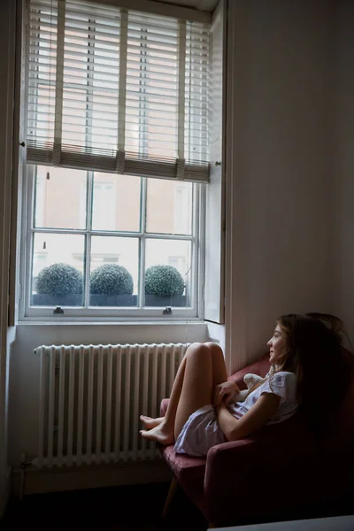 寝室の窓そばのアームチェアに立つ女の子 ロイヤリティフリーのストック画像