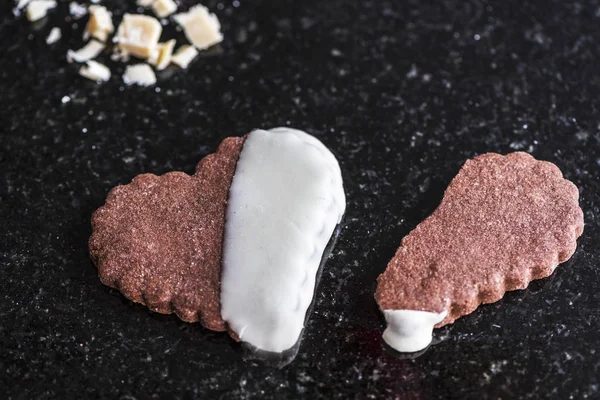 Whole heart shaped chocolate cookie with a broken heart shaped brown cookie on a black marble counter, close up, st. valentine\'s special cookies