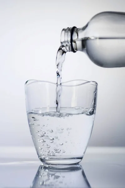 A glass of water pouring from a glass of bottle on a white background, close up, isolated.