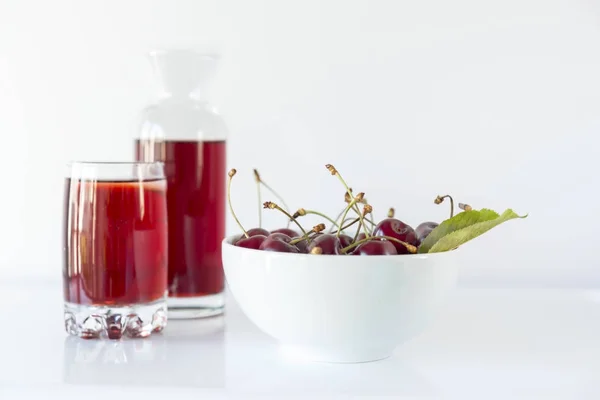 A bowl of cherry with a carafe and a cherry juice on a white background, close up, macro