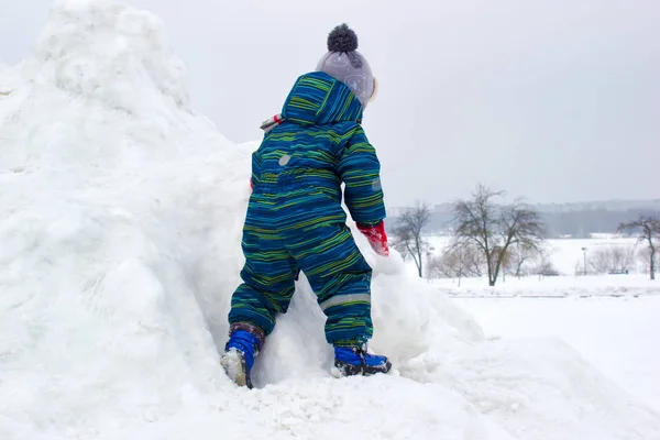 歳の子 男の子は雪に覆われた丘を登っています 彼はカラフルな冬の服を着ています 背面から見る — ストック写真