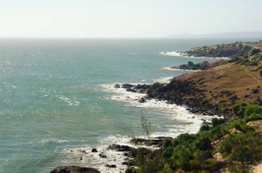 Güneşli deniz manzarası. Kayalık sahil, çöl bitki örtüsü ile. Fırtınalı dalgalar sörf. Uzak ufuk. Asya, Vietnam, Phan Thiet, MUI Ne köy. Güney Çin Denizi, Pasifik Okyanusu.
