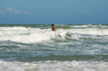 Biri su göğsünde duruyor ve sörf büyük dalgalar ortasında banyoları. Okyanus üzerinde açık gökyüzü güneşli bir gün.
