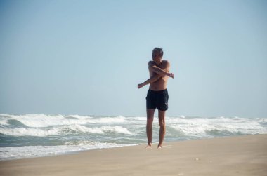 Bir adam Yüzme şort kumlu bir plaj boyunca yürüyüş ve egzersizleri ile birlikte büyük dalgalar sörf yapıyor. Açık gökyüzü, güneşli bir gün.