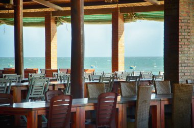 Sahilde bir gölgelik altında bir kafede tablolar. Kafeden görüntülemek