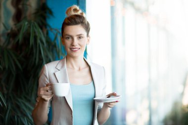 Fincan çay veya kahve ve çay-tatilinde ofiste kameraya bakarak uçan daire ile genç kadın Yöneticisi