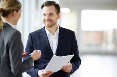 Genç adam şık takım elbise ve meslektaşı kağıt veya sözleşmenin koşulları tartışıyor