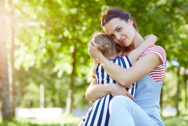 Küçük kızını sarılma ve güneşli günde kamera doğal ortamda bakarak Genç Anne bakım