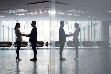 Kendine güvenen genç girişimci geniş ofis lobisinde, duvar yansıması onu tebrik ederken erkek iş ortağı el sallayarak tam uzunlukta portresi