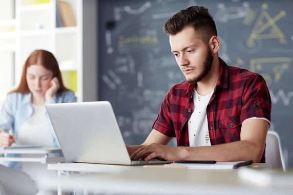 集中十几岁的学生坐在办公桌前的笔记本电脑 而在网上寻找必要的信息 — 图库照片