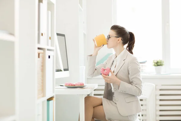 Young Hungry Businesswoman Drinking Coffee Yellow Mug Eating Fresh Donuts — Stock Photo, Image