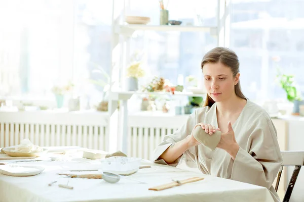 テーブルに座って セラミック粘土からマグカップをワークルーム 灰色のローブの若い創造的な女性 — ストック写真