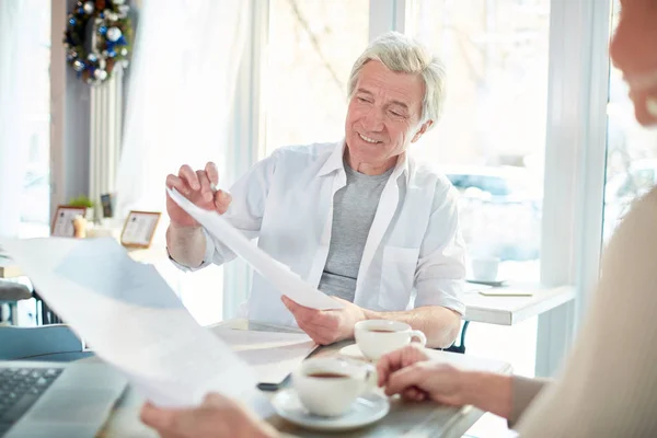 Senior confident businessman pointing at paper or contract while negotiating with client or business partner