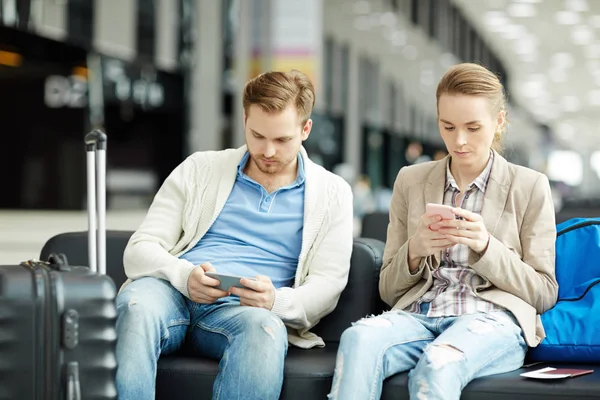 つの現代的な男と普段着のまま空港と彼らのスマート フォンでの検索のラウンジで座っている女 — ストック写真