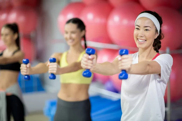 Wesoły Zdrowych Młodych Kobiet Hantlami Ćwiczenia Wyciągnął Ramiona Centrum Fitness — Zdjęcie stockowe