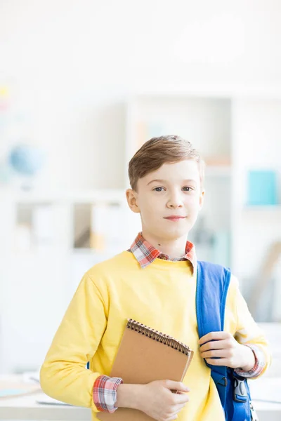 レッスンの前後に教室でカメラを見て黄色のセーターで巧妙な男子生徒 — ストック写真