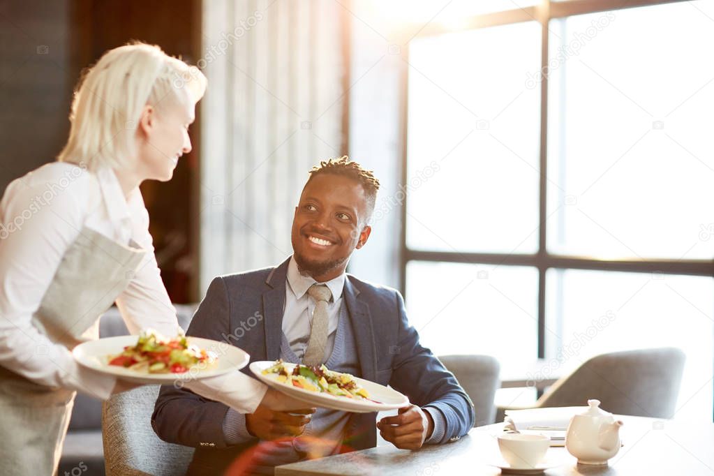Happy businessman taking two vegetable courses on plates brought by waitress