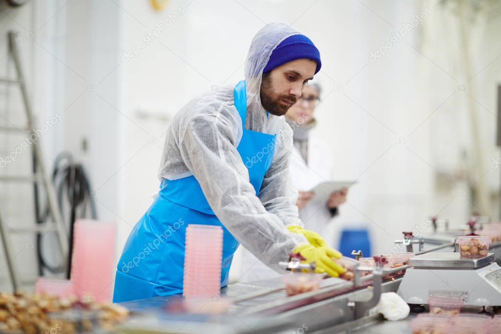 Young man in protective uniform working by production-line in seafood processing factory