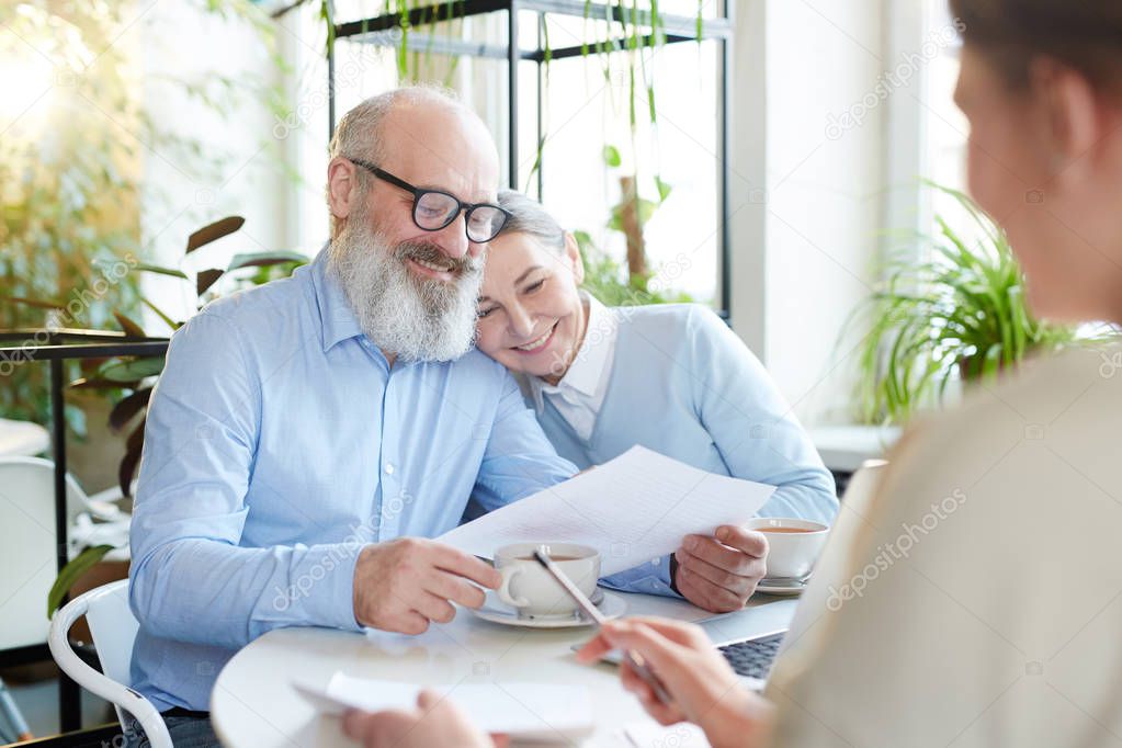 Mature man and woman reading points and terms of contract or agreement during meeting with agent in cafe
