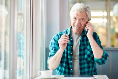 Komuta sizde kafede tabloya göre arama, çay içiyor ve kameraya bakarak smartphone ile gülümseyen