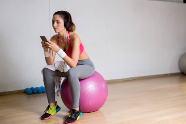 Çalma listesinden smartphone içinde spor giyim fitball sonu ve dinlerken oturan genç dinlendirici kadın izler