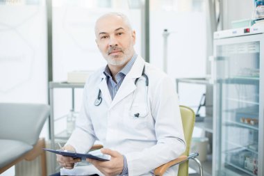 Tek tip koltukta oturan kliniklerde belgelerle çalışırken, kendinden emin olgun klinisyen