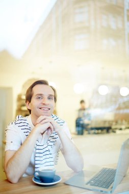 Laptop ve kahve ile masada oturan gülümseyen adam portresi