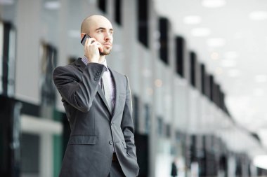 Ciddi genç iş adamı yanında smartphone modern Havaalanı lounge dururken konuşmaya resmi kıyafeti