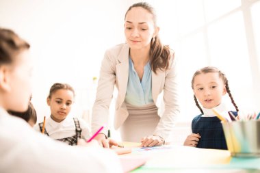 Onun schoolchlldren bir ders sırasında yardımcı öğretmen. Onlar masada çizim