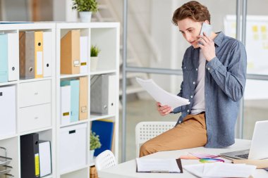 Telefonda konuşurken elinde belgelerle genç casual işadamı