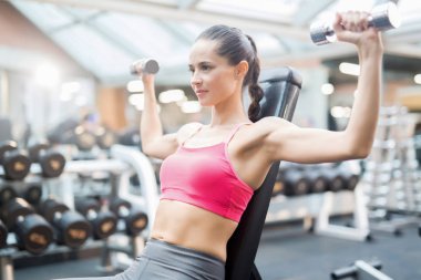 Kol kasları eğitim fitness merkezinde pompalama iki metalik dumbbells ile genç erkek