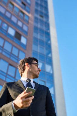 Kendine güvenen genç Yöneticisi bir kenara çağdaş iş merkezi arka plan üzerinde seyir smartphone ile