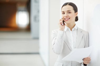 Duvar dibinde duran ve sözleşme noktaları ve şartlar bir müşteri için smartphone tarafından okuma elbiseli genç gülümseyen esmer