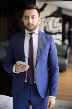 İş seyahati sırasında otel odasında kamera bakarak smartphone ile genç zarif çalışan