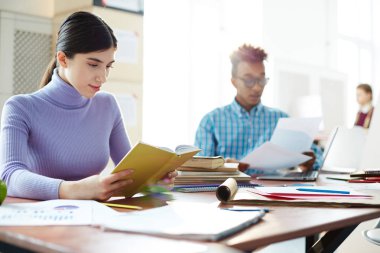 Groupmate arka plan üzerinde kitaplıkla ev ödevi hazırlarken kitap okuma ciddi kız öğrenci