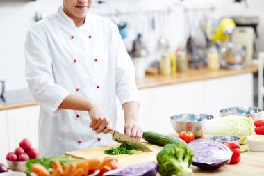 Genç şef iş yerinde pişerken sebze salatası veya çorba baharat için aromatik otlar kesme