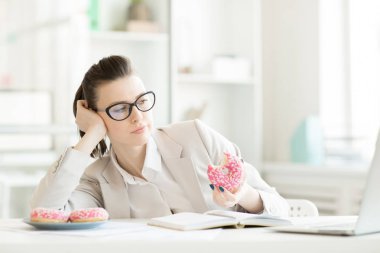 Lezzetli donuts yeme ve net bir şey tarafından Danışma laptop önünde otururken izlemek tembel genç iş kadını