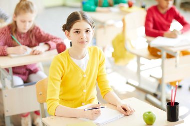 Ders işyeri tarafından otururken kameraya bakarak mum boya ile zeki kız öğrenci