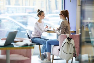 Pencere kafede otururken, rahatlatıcı ve yeni proje hakkında konuşmak genç üniversite öğrencileri