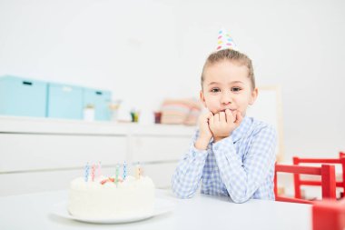 Doğum günü pastası önünde masa başına oturmuş, bu tatma ve kameraya bakarak sevimli küçük kız