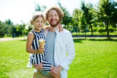 Sevgi dolu baba ve kızı kameraya güneşli yeşil çim arka plan üzerinde seyir