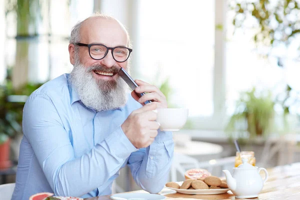 眼鏡と青いシャツとクッキー ティーポット テーブルでカメラ目線で幸せな成熟した男 — ストック写真
