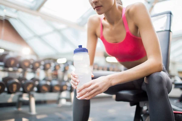 Young active woman with plastic bottle of water relaxing between trainings in fitness center