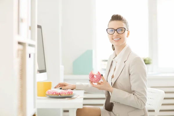 Jonge Glimlachende Zakenvrouw Met Donut Camera Kijken Tijdens Lunch Pauze — Stockfoto