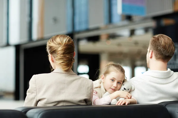 空港ラウンジで彼女の両親の間に座ってカメラ目線かわいい小さな旅人 — ストック写真