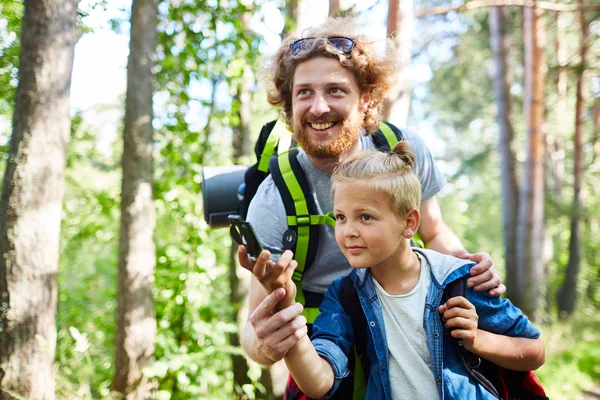 快乐的年轻人和他的儿子与指南针在森林里在旅途中定向 — 图库照片