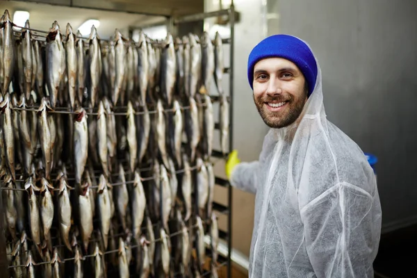 Young smiling fish factory worker in protective uniform looking at camera during work